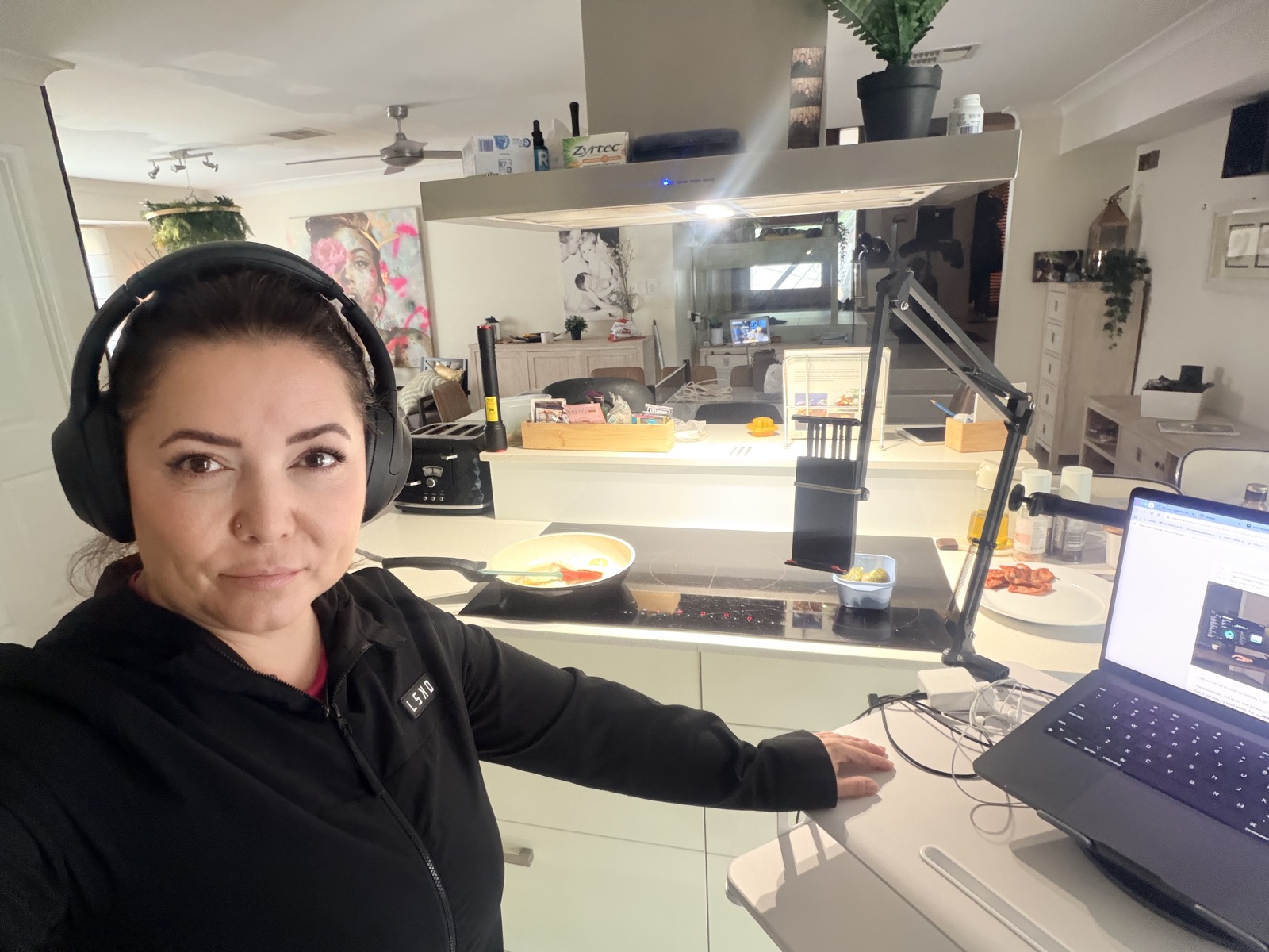 Julia at her kitchen counter in a black hoodie, cooking while working on her laptop