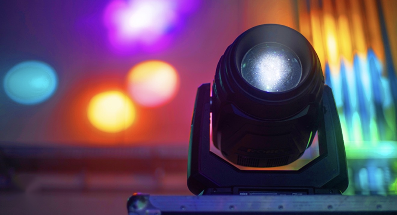 Close-up of a moving head lighting fixture on a road case with colorful blurred lights behind it