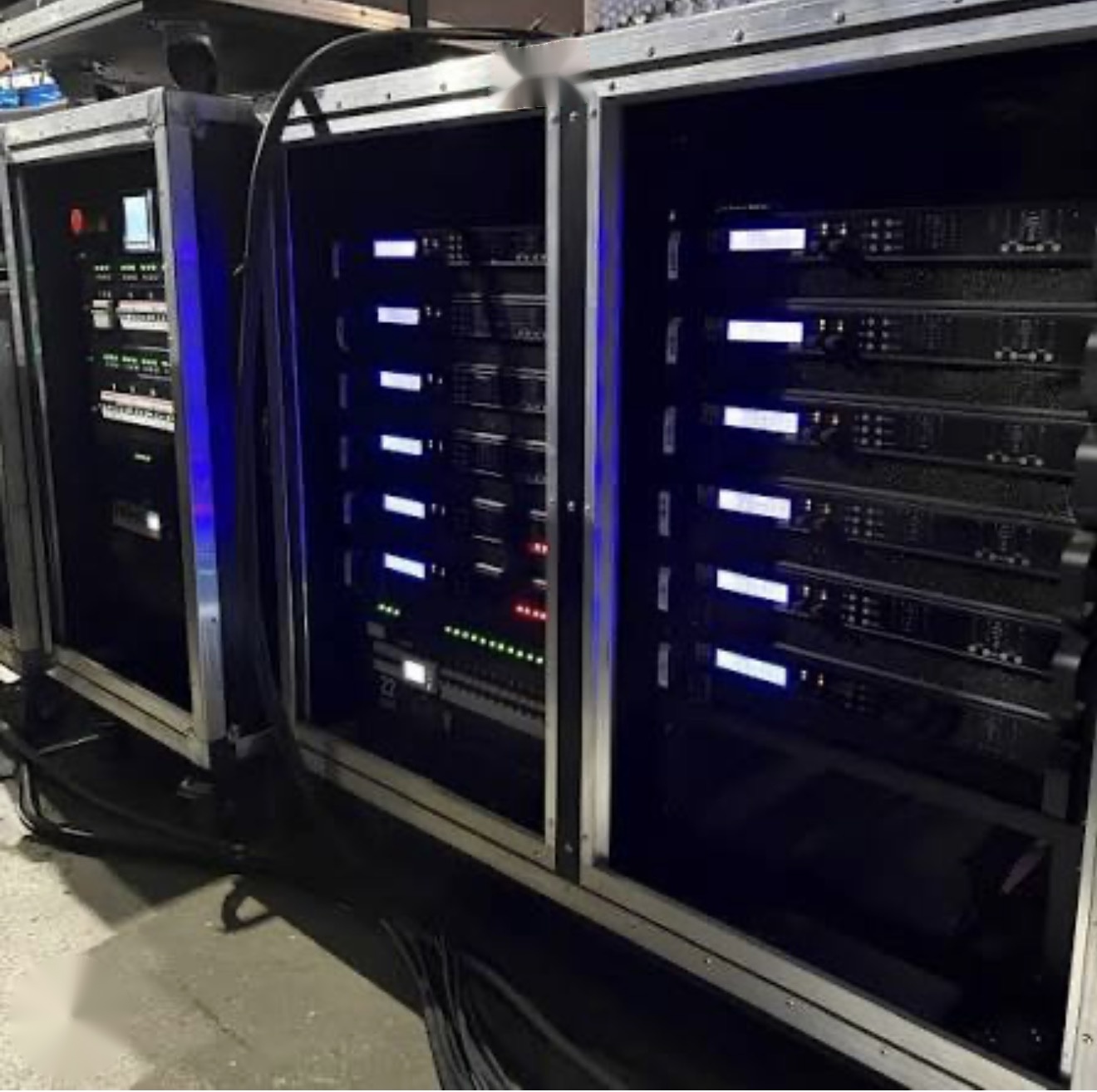 Three road-case equipment racks with amplifiers and processors showing lit displays