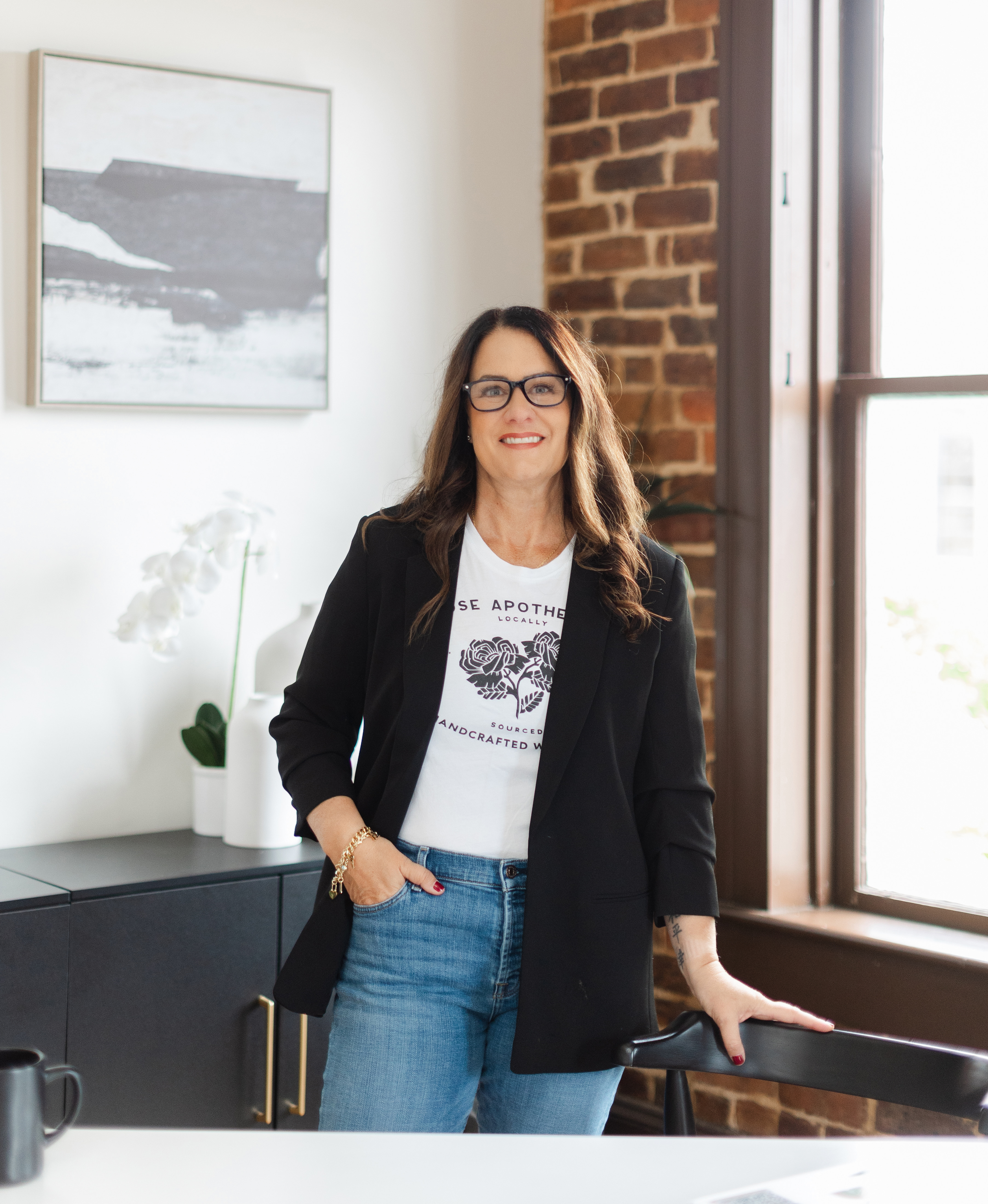 Sarah Price smiling, standing in her office in a black blazer