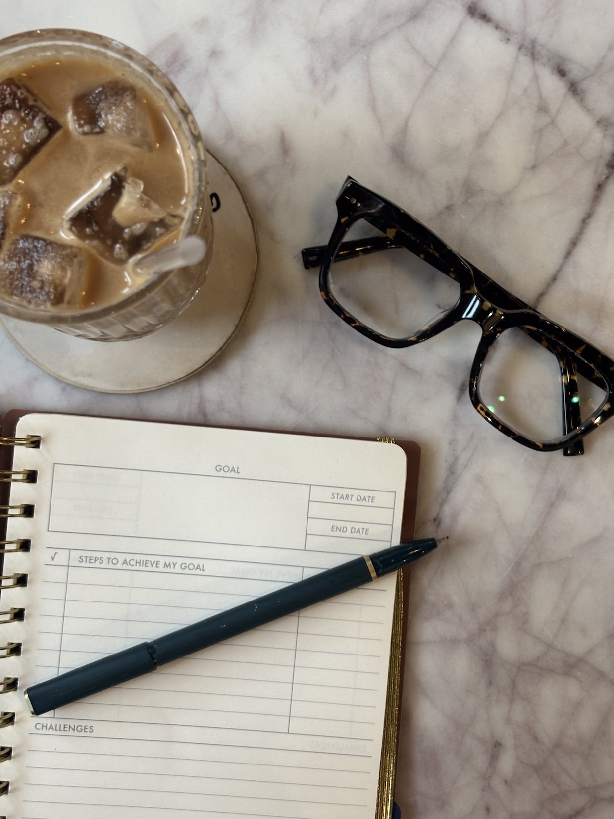 Planner open to a goals page next to a coffee and glasses
