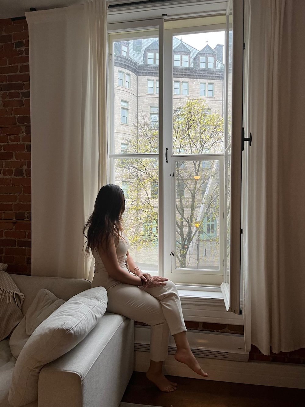 Woman sitting by a large window, looking out at the city