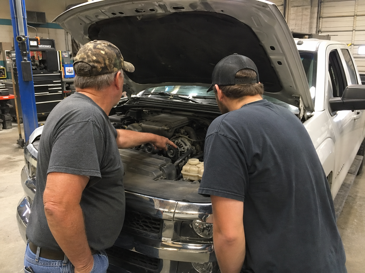 Father and son looking into truck engine bay together in shop