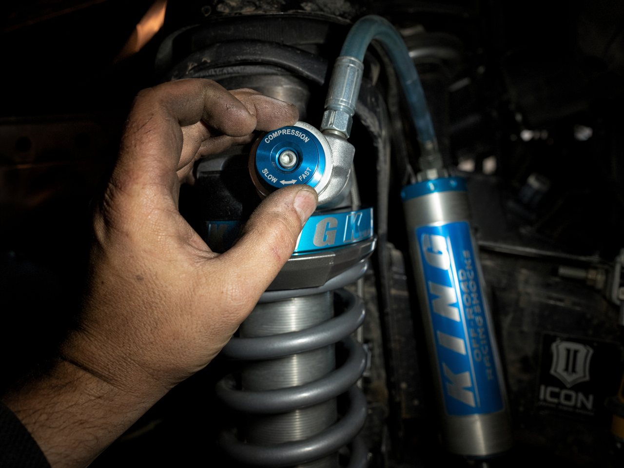 Mechanic hands adjusting compression damping dial on installed coilover shock