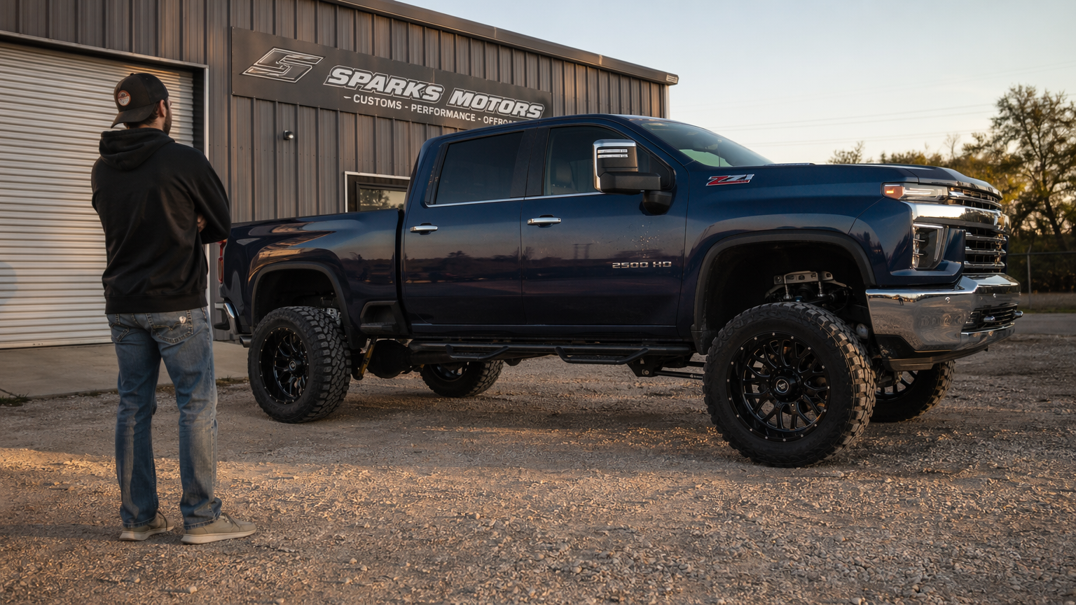 Customer standing beside completed lifted truck build in shop parking lot