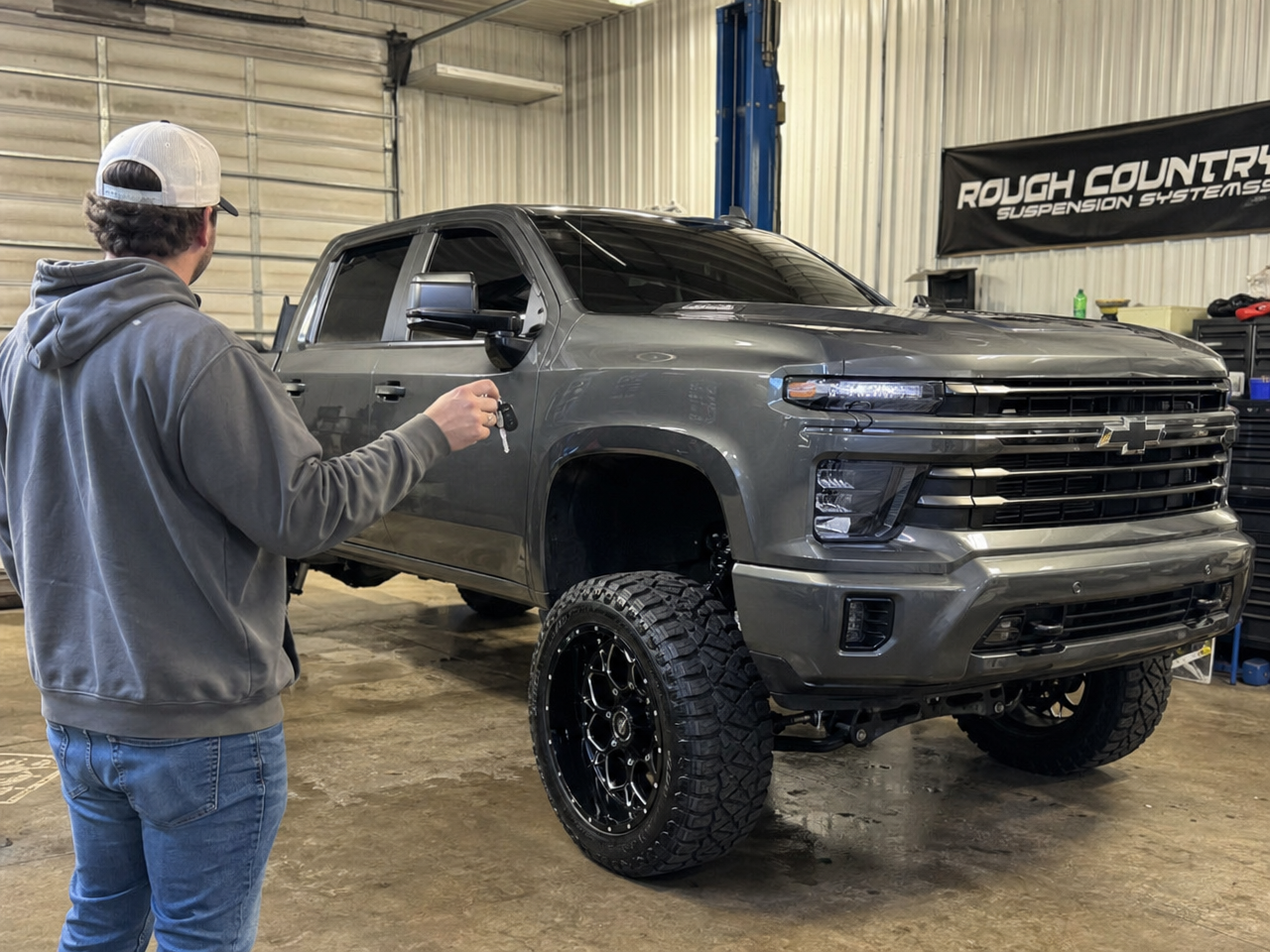 Truck owner holding keys beside freshly completed lifted truck in shop bay at delivery