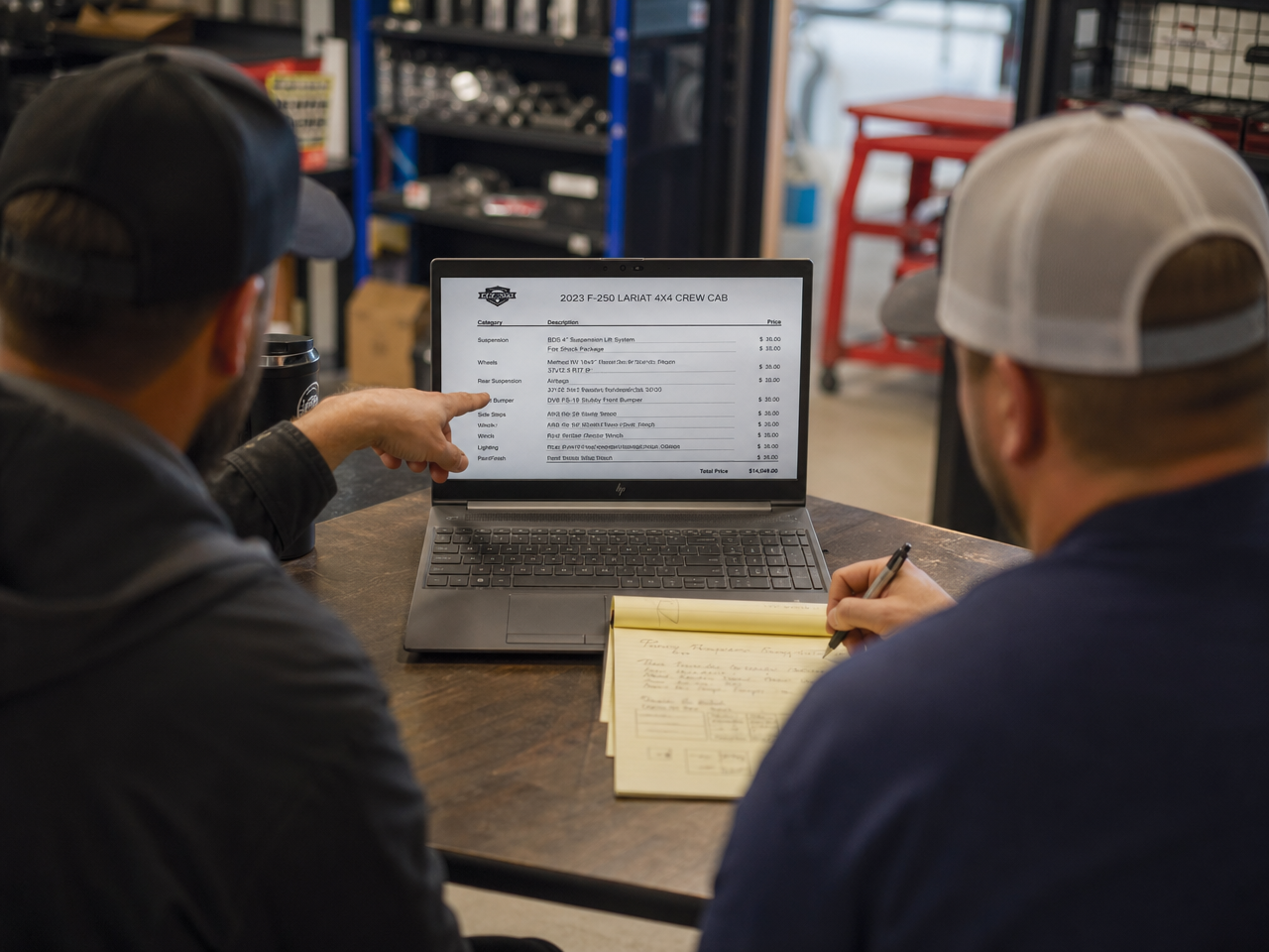 Shop owner and customer at desk reviewing truck build spec during consultation