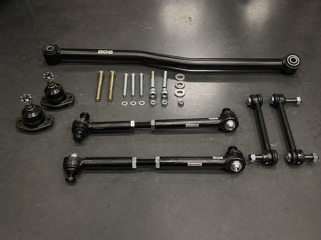 Front end components flat lay showing track bar ball joints and tie rod ends on shop floor