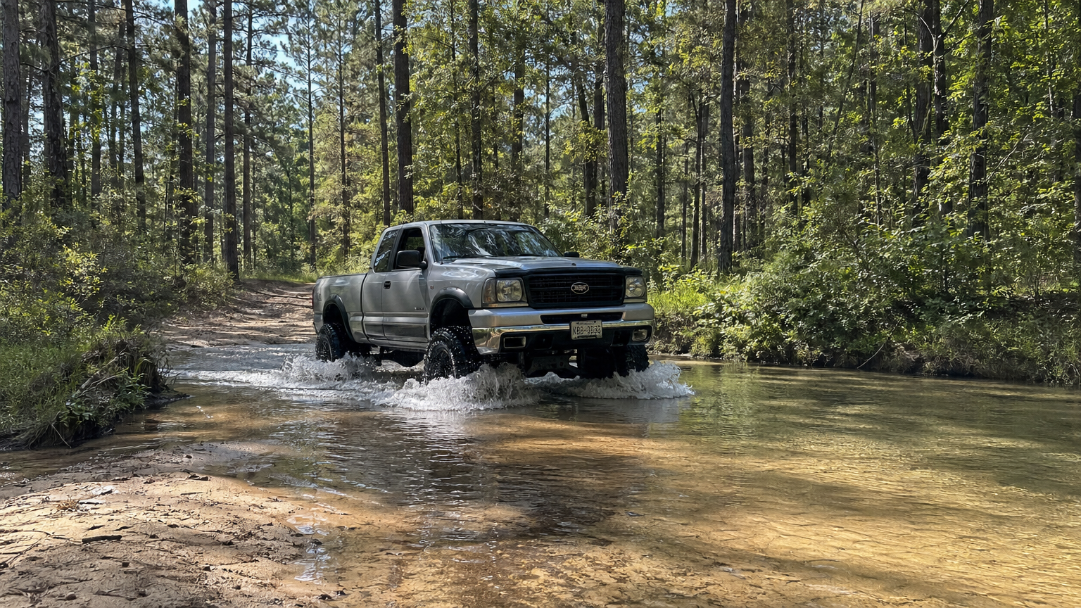 Lifted truck crossing a sandy creek in East Texas pine forest