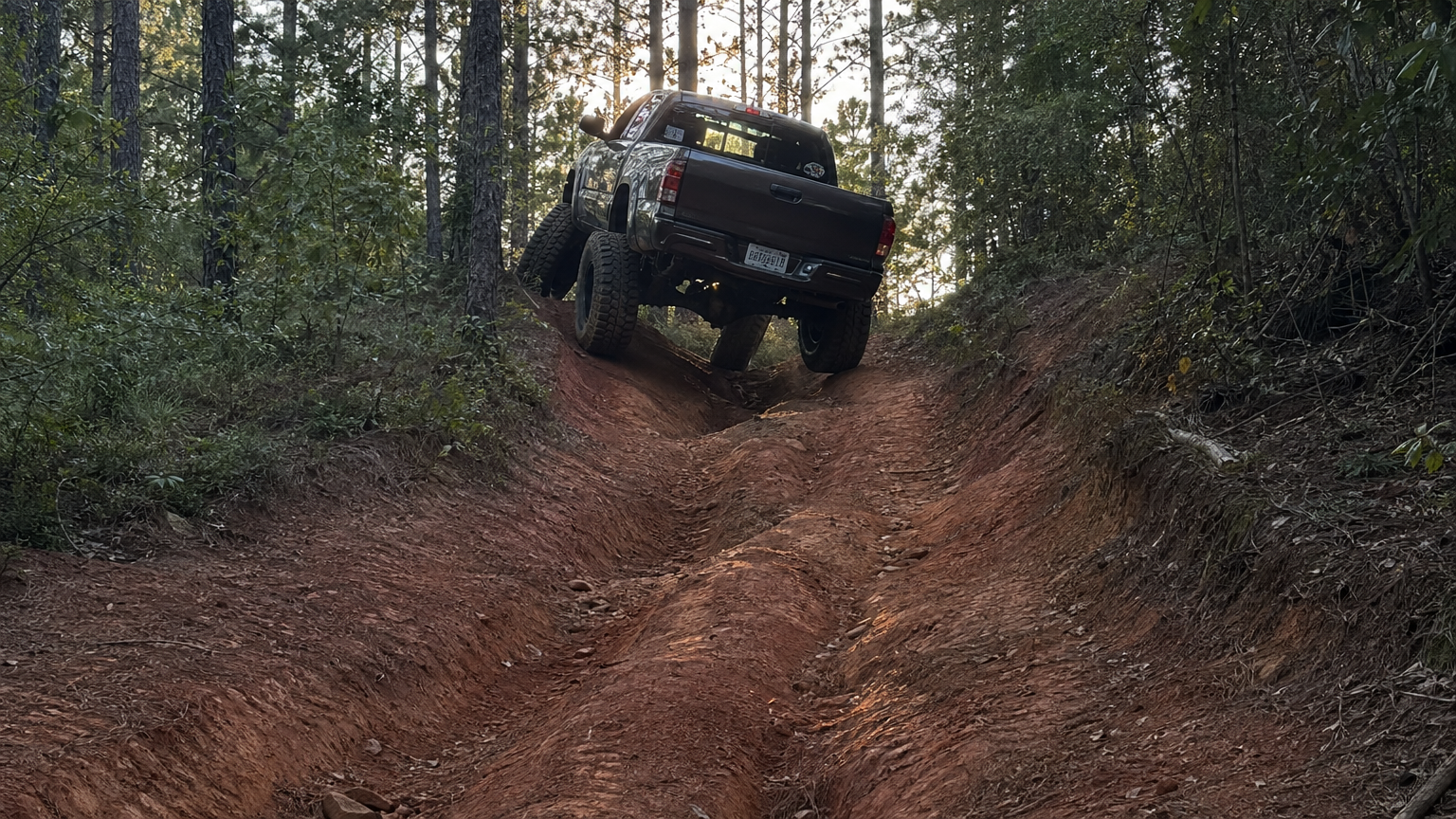 Lifted truck climbing steep rutted hill trail through East Texas piney woods