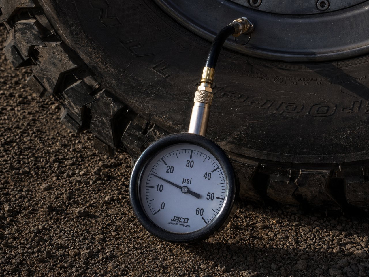 Tire pressure gauge on aired-down mud terrain tire showing low PSI reading on trail