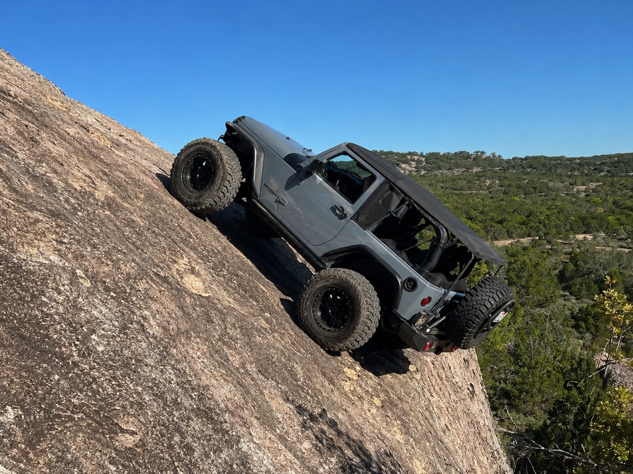 Lifted Jeep Wrangler climbing steep dry granite rock face in Texas Hill Country terrain