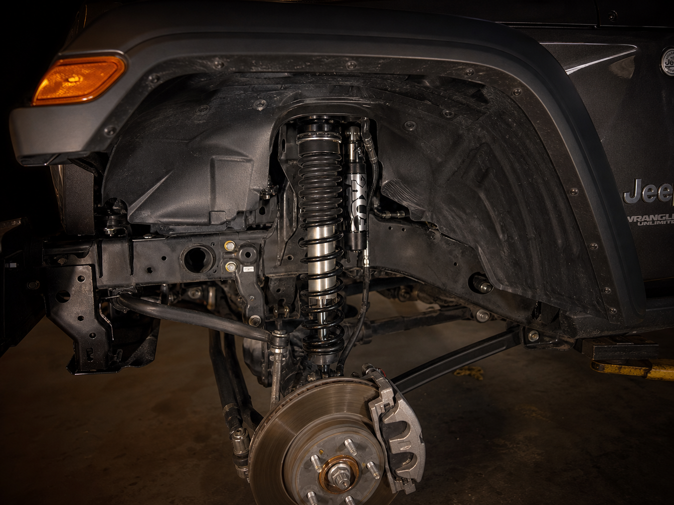 Jeep Wrangler JL coilover visible through wheel opening mid-articulation on rocky Texas trail