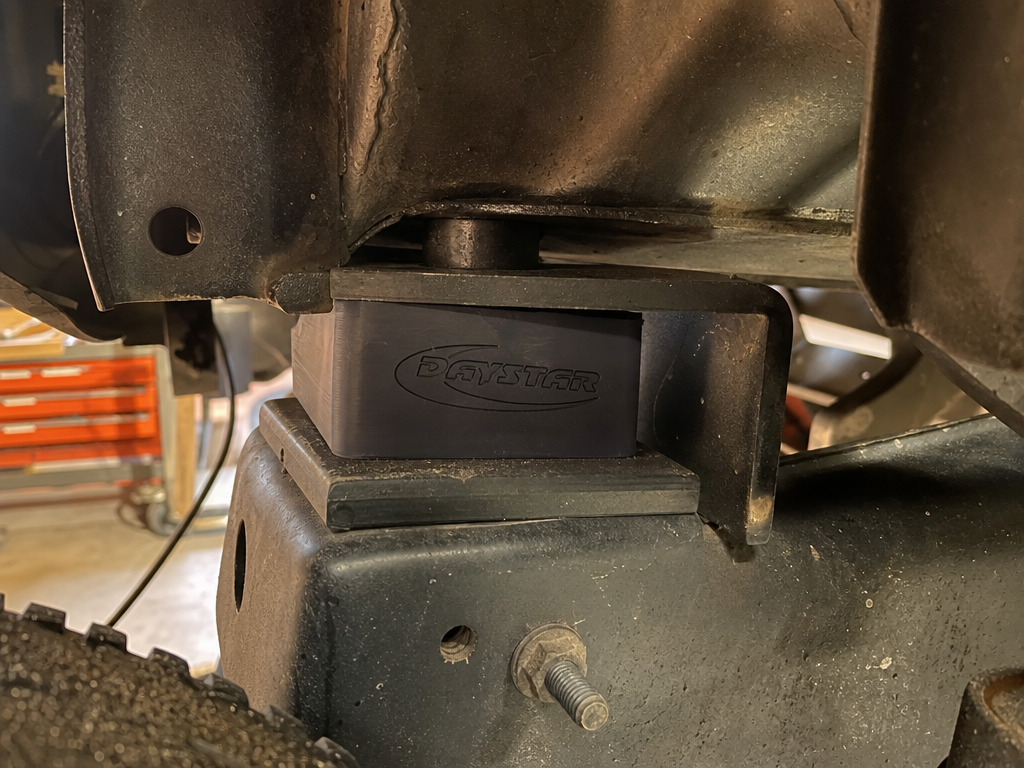 Body lift spacer block installed between truck body and frame at Iron Ridge Off-Road Houston