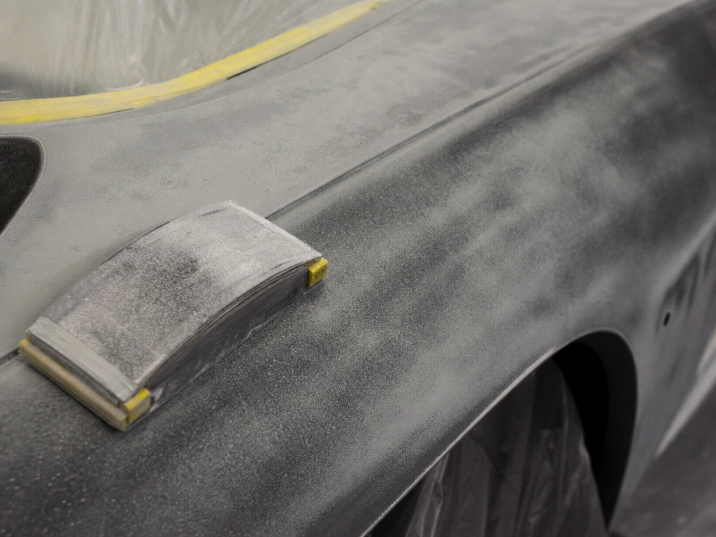 Guide-coat block sanding on a classic car panel during paint preparation