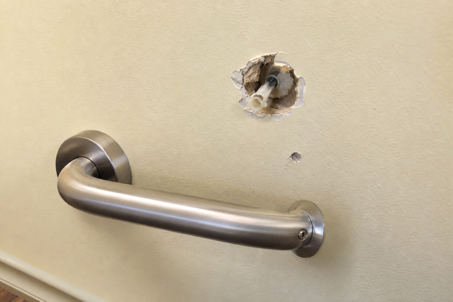 A grab bar pulled loose from drywall with a torn anchor hole