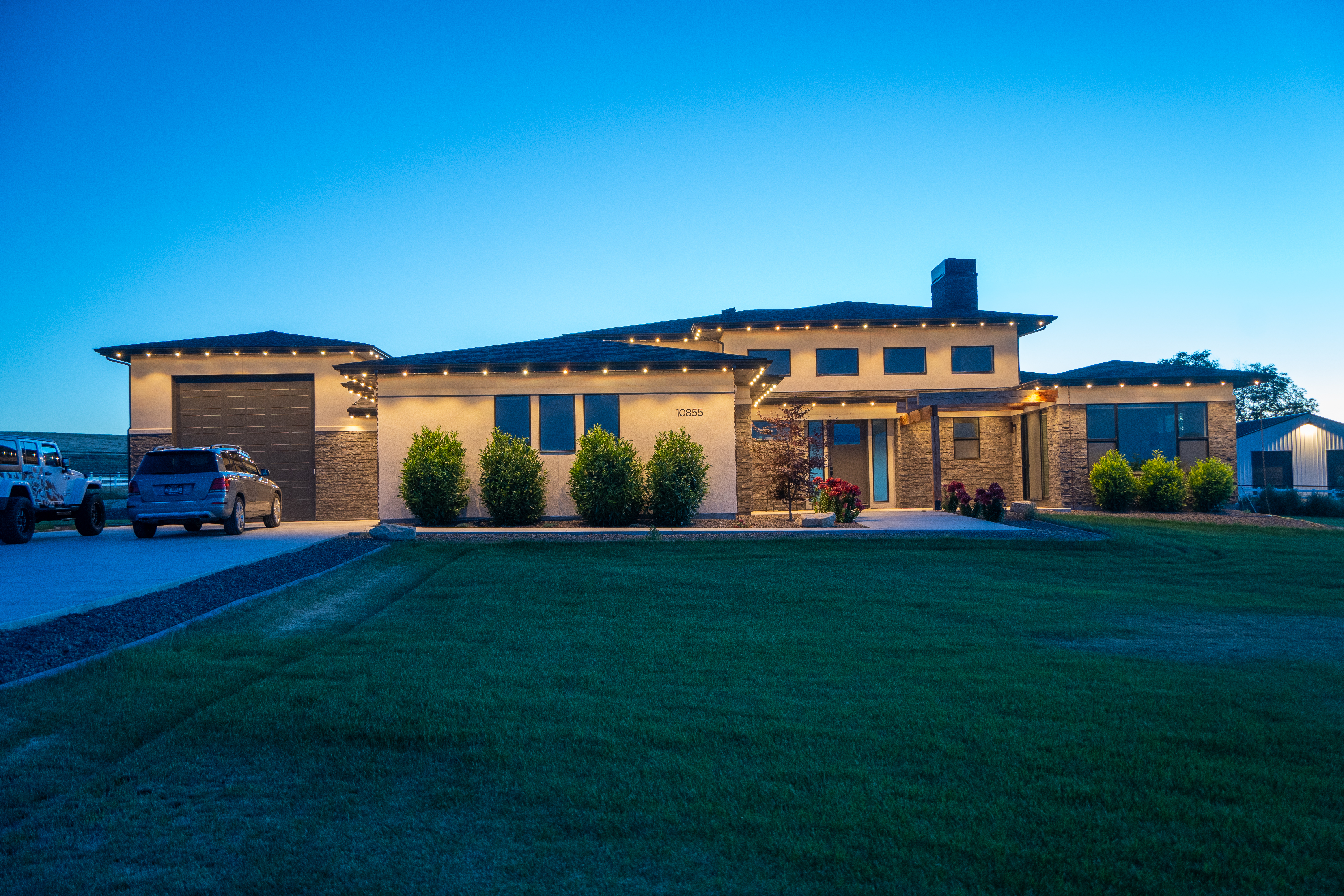 Same home at dusk with warm white permanent lights tracing the roofline