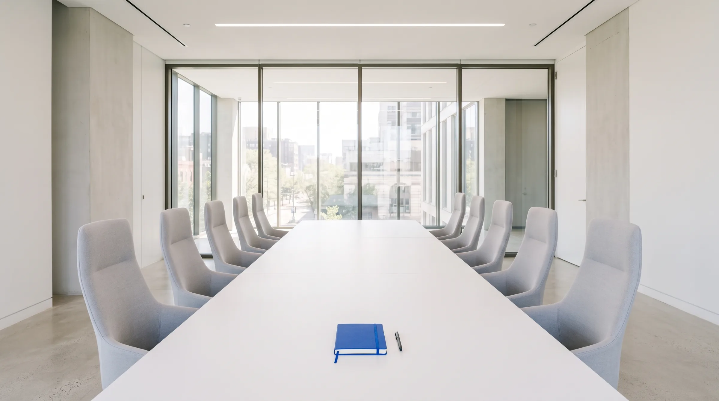 A quiet conference room with a long white table, glass walls and one blue notebook on the table