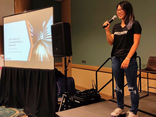 Rose Song Wang speaking on stage while standing on InMotion hovershoes