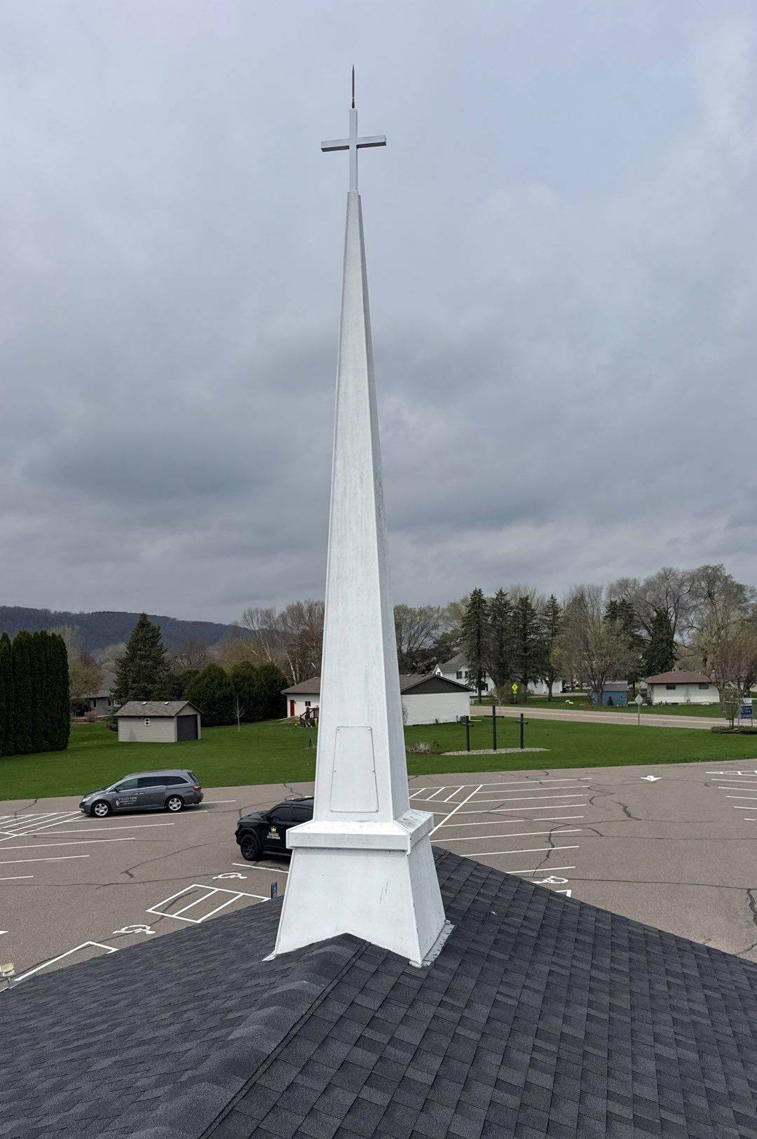 White steeple on the new gray shingle roof of Valley View Assembly of God in Lake City, MN, about 13 miles up the Mississippi from Wabasha, with the river bluffs behind it, April 2026