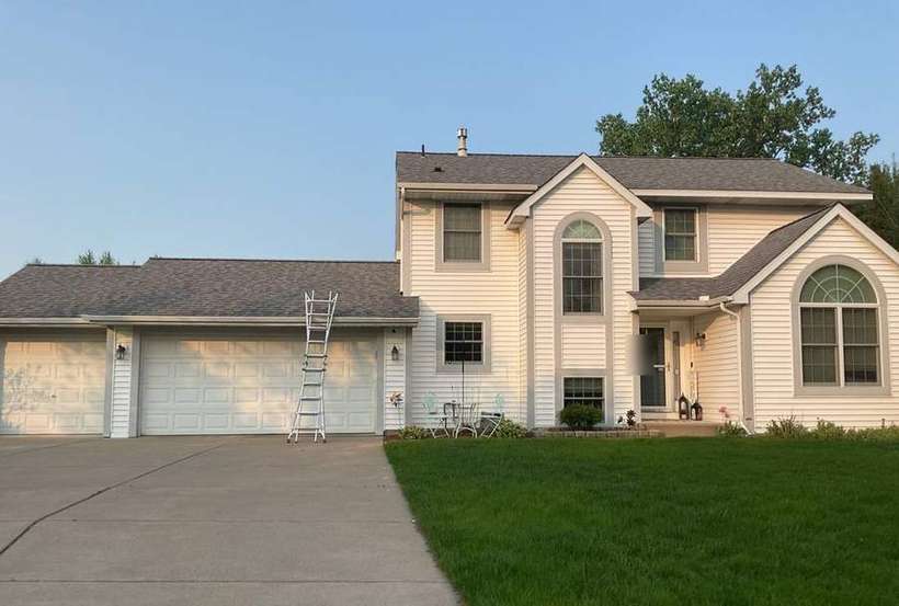 Two-story Woodbury home with stacked gables, an arched-window bump-out and a three-car garage, photographed with a ladder set during a May 2023 roof inspection