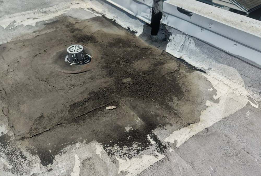 Roof drain surrounded by stained, peeling membrane coating at a parapet wall on Bethany Lutheran Church in Lake City, MN, April 2026