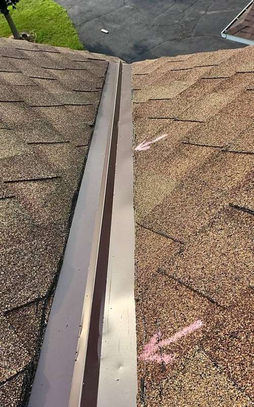 Dented metal valley flashing marked with pink chalk arrows on a Cottage Grove roof, July 2023