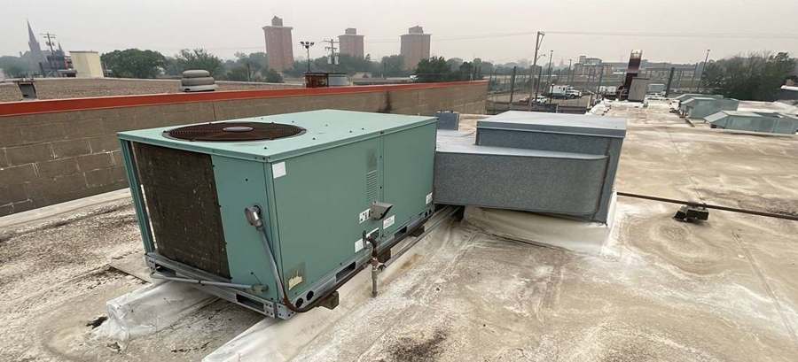 Rooftop HVAC unit and ductwork on the coated flat roof of the Cabooze on Cedar Avenue in Minneapolis, with the West Bank skyline behind, June 2023
