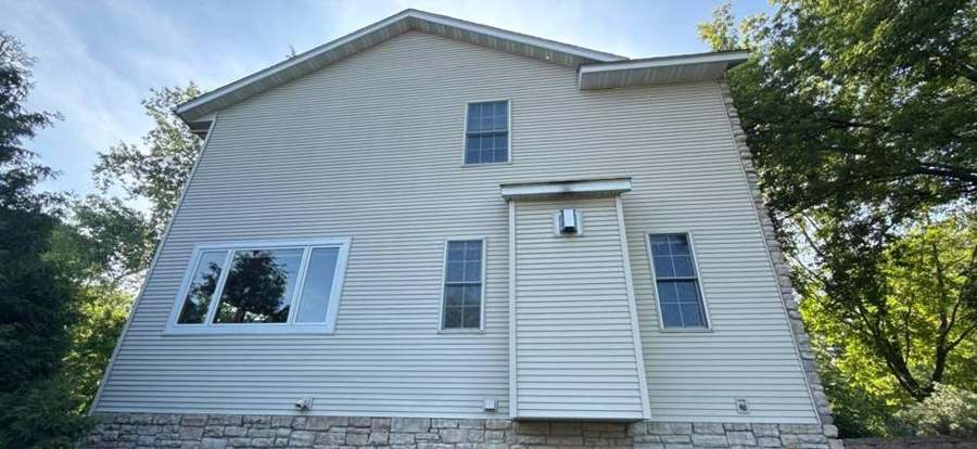 Side wall of a two-story Shoreview home with vinyl siding over a stone base, photographed by Repair King before new siding, May 2026