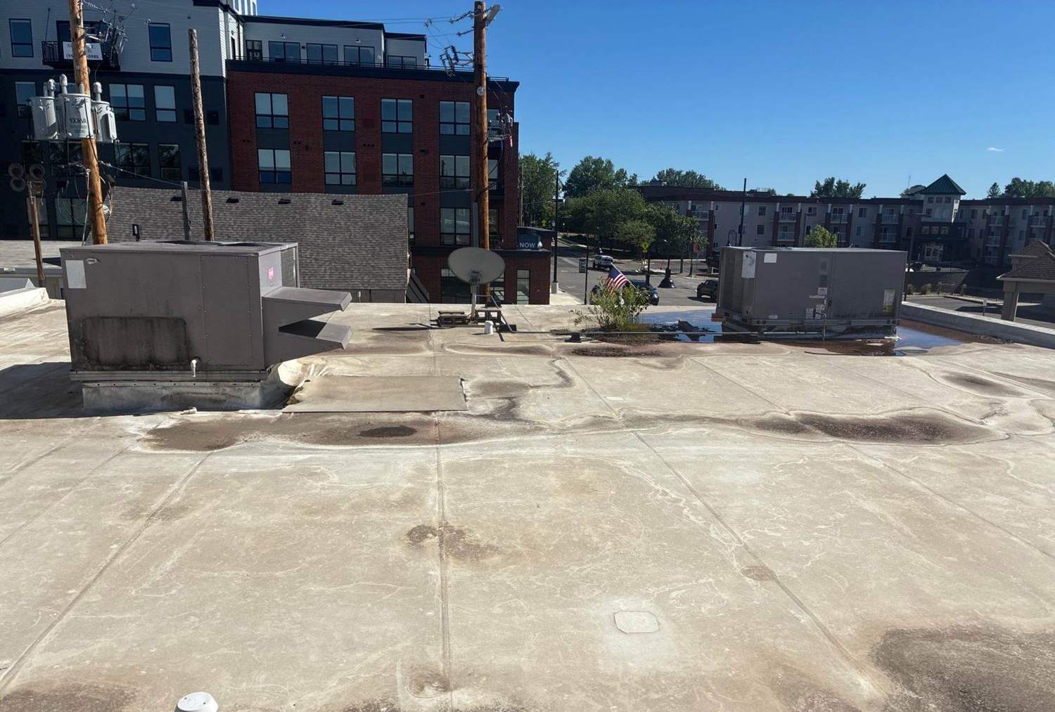 Wide view of a low-slope commercial roof in downtown Waconia, MN with rooftop HVAC units and an apartment building beyond, photographed by Repair King in 2026