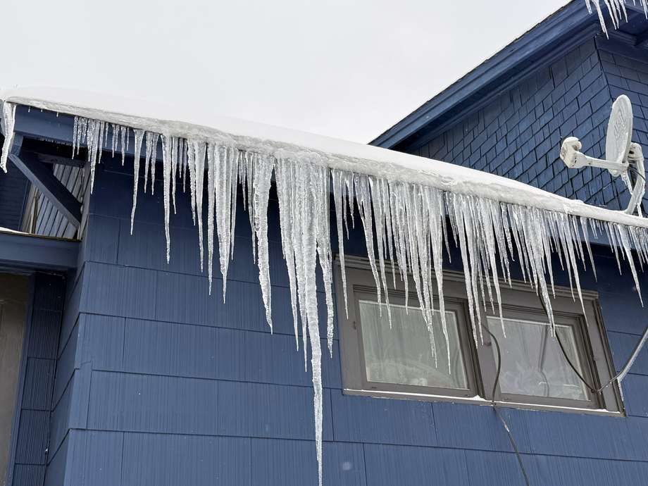 Heavy icicles hanging across the full length of a roof edge on a blue house