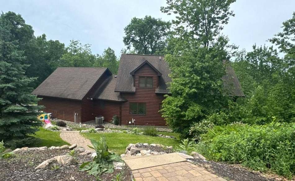 Log cabin home in Crosslake photographed from the garden path during a roof inspection, June 2024