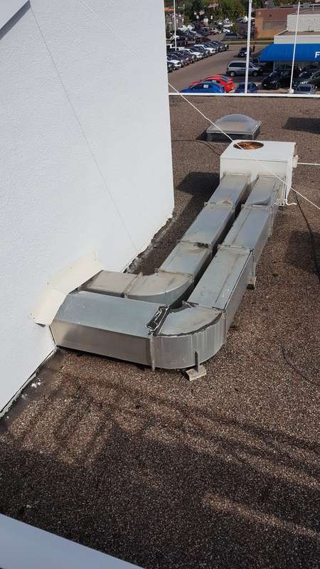 Old ductwork running across the gravel roof at the Forest Lake dealership before the replacement