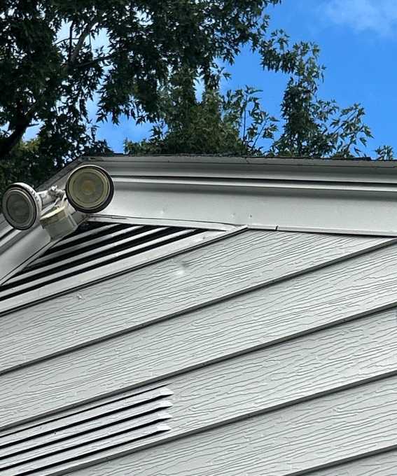 Gable end with louvered vent, gray lap siding and flood lights on a single-story home on 4th Avenue in Newport, MN, September 2025