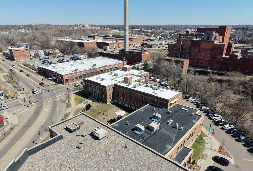 Drone view over HOPE Community Academy's flat roofs on Payne Avenue in St. Paul, MN, with a smokestack and brick buildings behind, April 2026