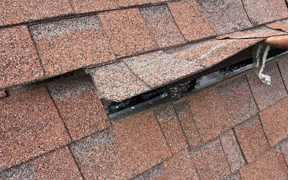 Wind-lifted shingle tab with a broken seal strip on a Chanhassen roof, September 2025