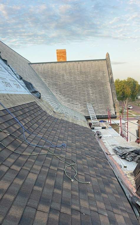 New brown architectural shingles installed on one slope of St. Paul's Lutheran Church in St. James, MN, with the old gray roof still visible on the next slope, July 2023