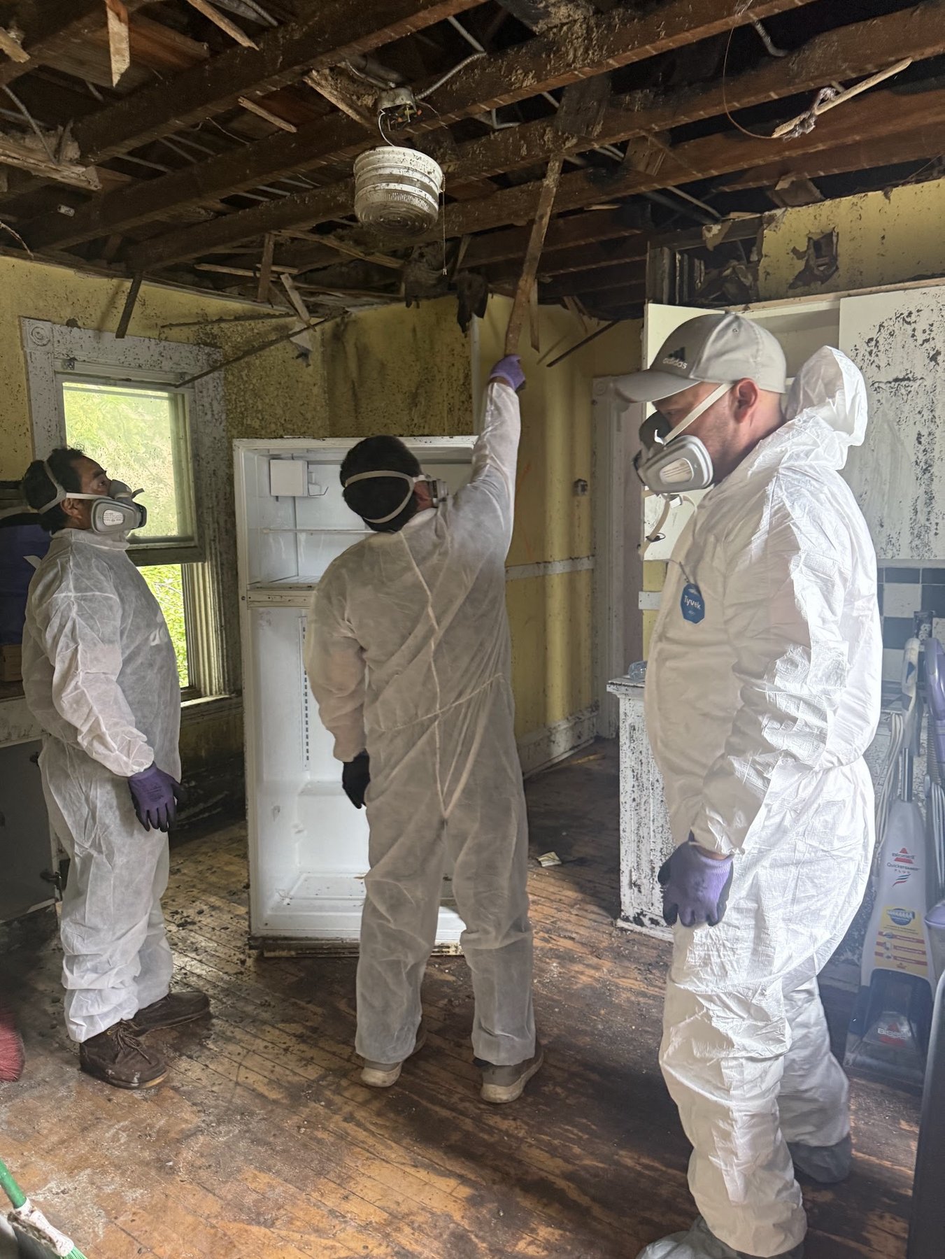 Crew in Tyvek suits and respirators assessing a fire-damaged kitchen