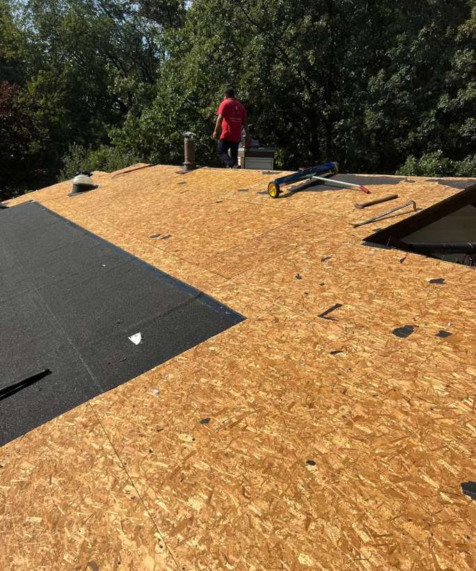Repair King crew member on a Lakeville roof torn down to the OSB deck, with the first underlayment rolled out, September 2023