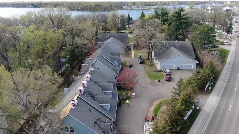 Drone view of a townhome row in White Bear Lake, MN, with one section torn off and shingle bundles staged on the finished side during a Repair King re-roof