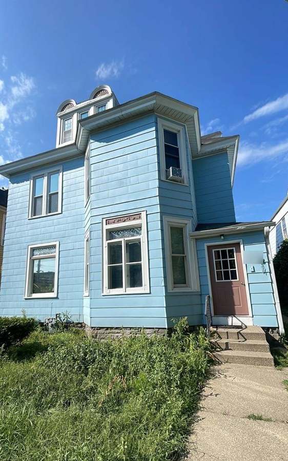 Light-blue three-story rental house with an arched dormer in the Elliot Park neighborhood of Minneapolis, photographed during a storm inspection in August 2023