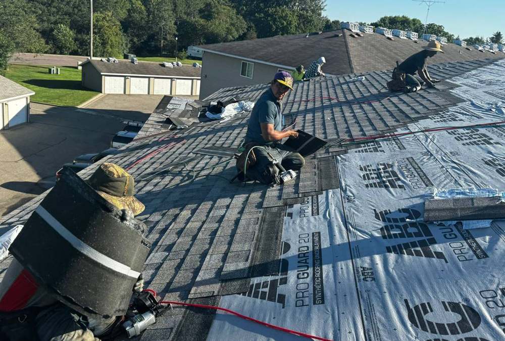 Crew laying synthetic underlayment on the Ridgedale Square roof in Hutchinson, with the garages below, August 2024