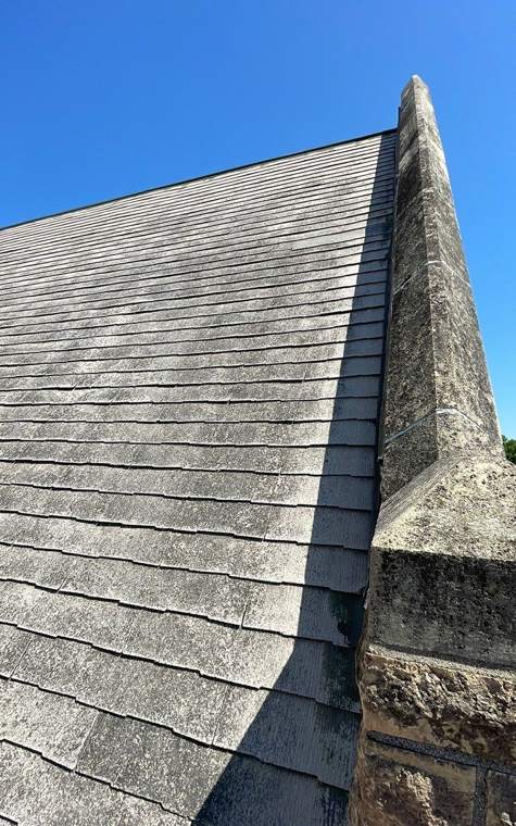 Steep old slate-style shingle roof meeting the stone gable of St. Paul's Lutheran Church in St. James, July 2023