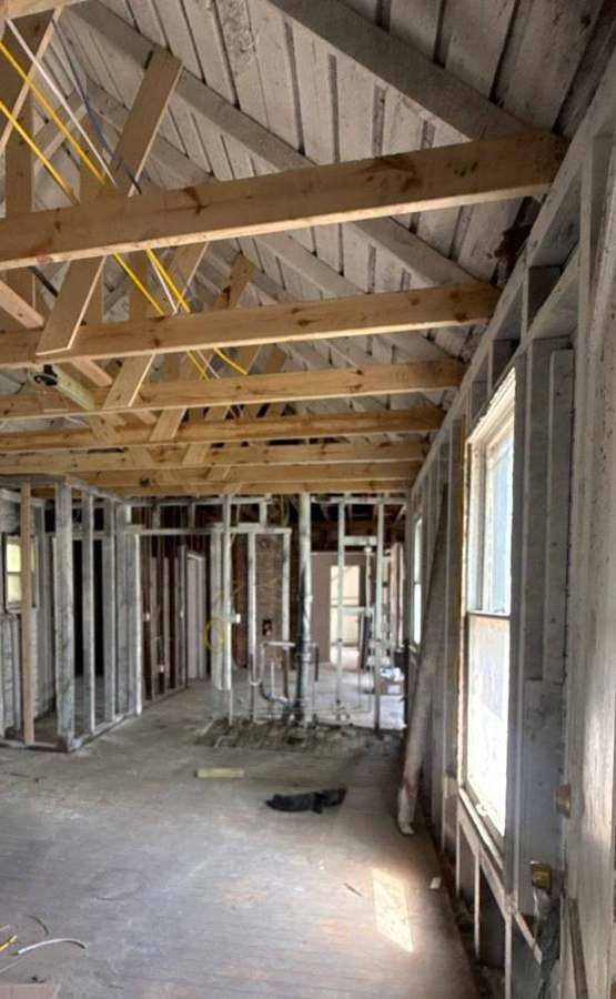 Interior of a south Minneapolis house taken down to the studs during a fire rebuild, with new framing lumber under the original board roof deck, May 2026