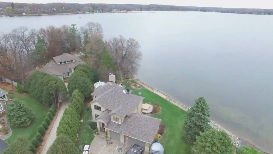 Drone view of a lakefront home on Forest Lake, MN during a Repair King re-roof, with the lake and far shoreline behind it
