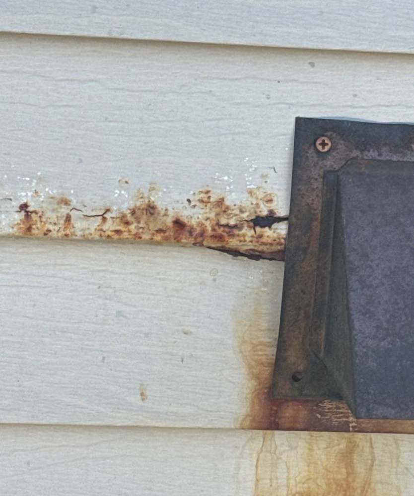 Rusted exhaust vent hood staining the siding on a Hutchinson apartment building, August 2024