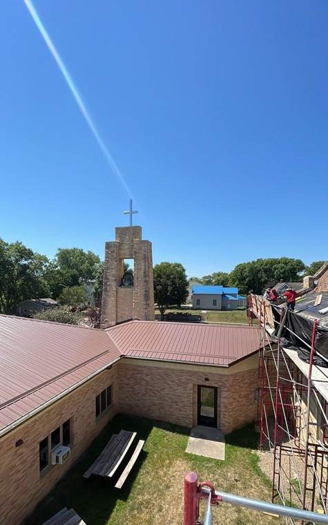 Stone bell tower and red metal wing roofs of St. Paul's Lutheran Church in St. James, MN, seen from the scaffolding during Repair King's July 2023 re-roof