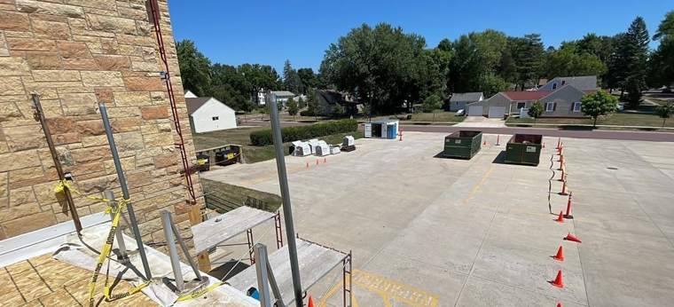 Fall-protection anchors and scaffolding at the stone wall of St. Paul's Lutheran, with safety cones on the lot, July 2023