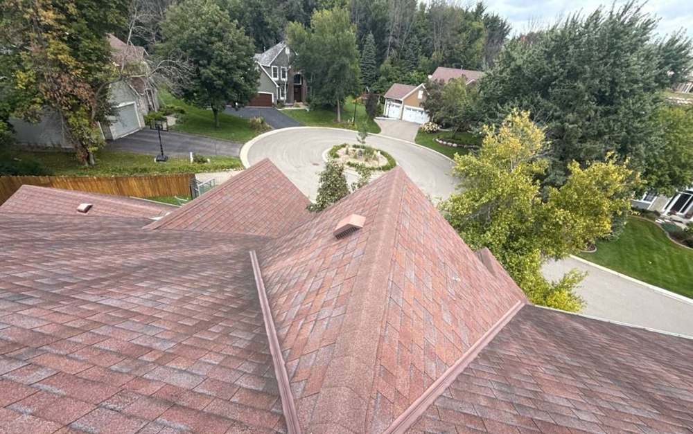Drone view over a reddish-brown shingle roof and a wooded cul-de-sac in Chanhassen, MN, during a Repair King inspection in September 2025