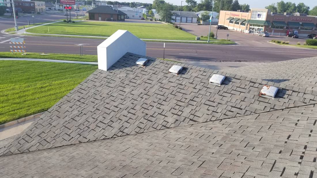 Shingle roof of Mega Coin Laundry in Fairmont, MN, with its row of box vents and the parking lot and East Blue Earth Avenue businesses beyond